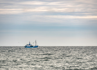 Small single fishing boat at the open sea with scenic sky.