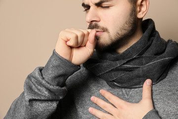 Handsome young man coughing against color background