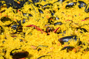 Close up of traditional Spanish paella dish freshly cooked in a large traditional black frying pan at a street food festival, ready to eat seafood, side view
