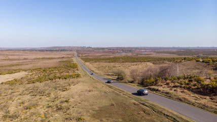 Aerial view of the New Forest National Park with heathland, lake, road, cars and cyclist under a majestic blue sky.