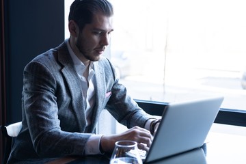 Full concentration. Good looking young man in full suit using computer while sitting in the cafe