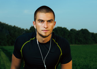 Fototapeta premium guy brunette in gym clothes. training in the field. listening to music on headphones through the phone