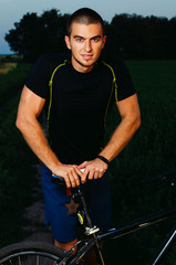 Fototapeta premium guy brunette in gym clothes. training in the field. sitting on the bike
