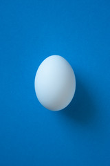 One single white egg on the bright blue background. White easter egg minimal composition. Easter symbol.