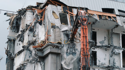 Excavator destroys the old building. Demolition work, pieces of concrete and reinforcement fall down