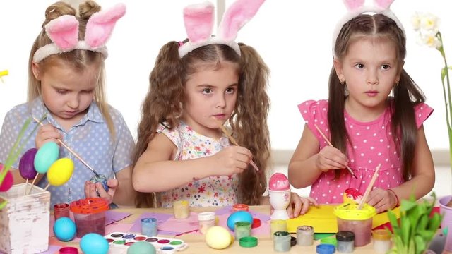 Happy children wearing bunny ears painting eggs on Easter day. Little girls preparing for the Easter.
