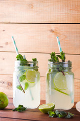 Mojito and mint on wooden background. Refreshing cocktail with lime and fresh mint on wooden boards. Two jars with handles with a summer drink with citrus and ice. Homemade mojito