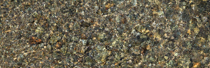 Mosaic texture with the golden shade (tint) in the sunrays. The bottom of the lake with pebbles under the clear water close-up, background