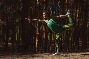 Beautiful young woman practices yoga asana Virabhadrasana warrior pose in the forest