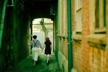 Fototapeta na wymiar two mimes holding hands go down a narrow alley