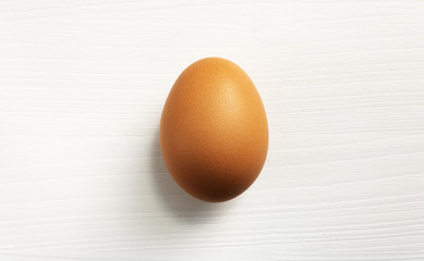 Isolated natural brown chicken egg on white wooden table with stronger shadow below the egg