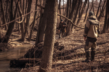 Hunting scene with hunters in camouflage going through dry forest during hunting season