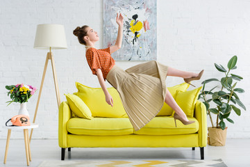 side view of elegant young woman levitating in air in living room