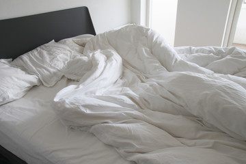 Messy white bedding sheets and pillows with wrinkles on bed  in a white bedroom