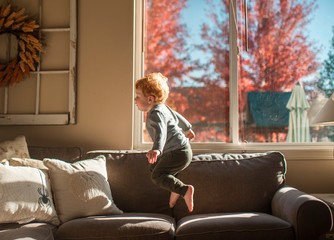 Toddler boy jumping on couch in living room