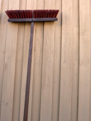 Ein Straßenbesen mit rauen roten langen Borsten und Holzstiel lehnt an einer Holzwand