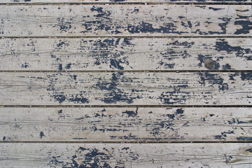 Gray planks of the old pier with peeling black paint and sand in the cracks