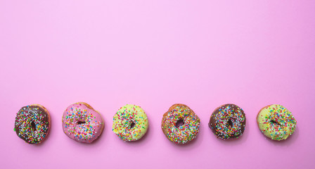 Donuts with colorful sprinkles on pink background, top view