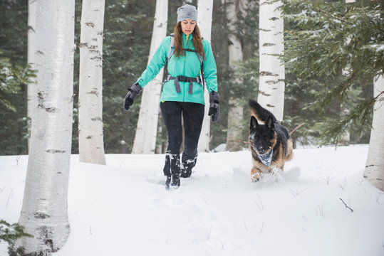 Woman and dog running on snow in woods