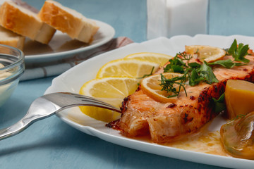 Baked salmon fillet medallion with salad of pickled vegetables and mushrooms on a white plate on a blue background