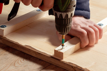 Male hands screw wooden blocks to the boards with a screwdriver