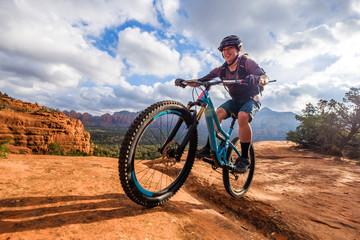 Female mountain biker riding along dirt trail against clouds, Sedona, Arizona, USA
