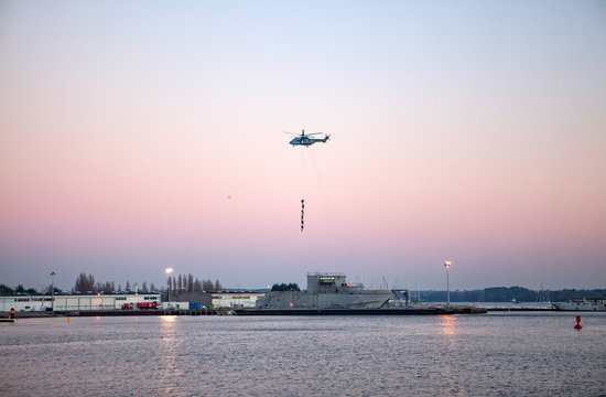 Helicopter hovering with six people above ship in harbor