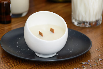 Handmade candle in white moon shape candlestick on black plate and wooden table. Front view. Healthy lifestyle concept;
