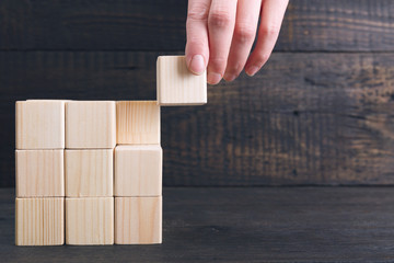 Woman's hand putting the final piece of wooden cube into place - achievement concept. Finish the project concept