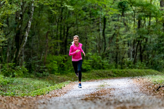 Woman in pink sweatshirt running along road in forest