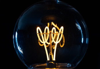 Classic retro incandescent edison light bulb: close up of the glowing filament - obrazy, fototapety, plakaty
