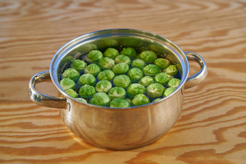 Stainless steel cooking pot with water and bunch of fresh harvested green brussels sprouts before cooking on wooden table. Light and healthy vegetarian or vegan dish full of  nutritions and vitamins.