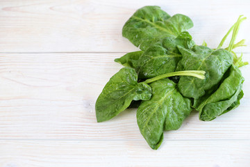 Green spinach leaves on a light wooden background