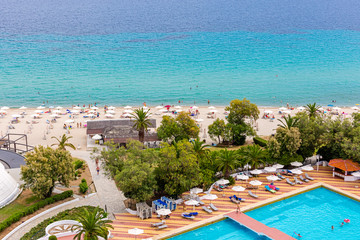 Plakat Beautiful view of outdoor swimming pool area with clear blue water, sunbeds and umbrella around. View of the sea shore with figures of tourists. Summer vacation and tourism concept