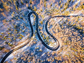 Winding road through the forest, from high mountain pass, in winter time. Aerial view by drone . Romania