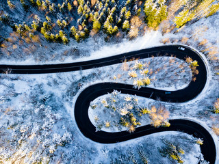 Winding road through the forest, from high mountain pass, in winter time. Aerial view by drone . Romania