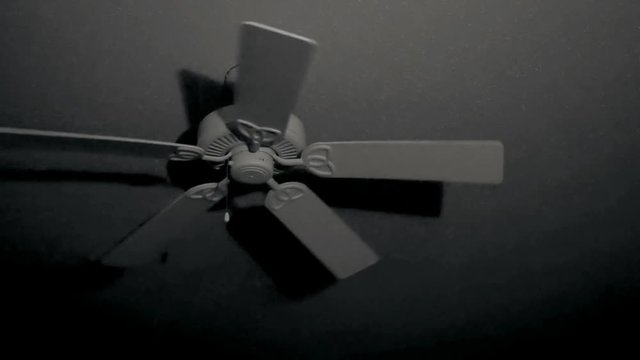 Rotating ceiling fan gradually slows down in dark room at night with shadows cast by a single light source.