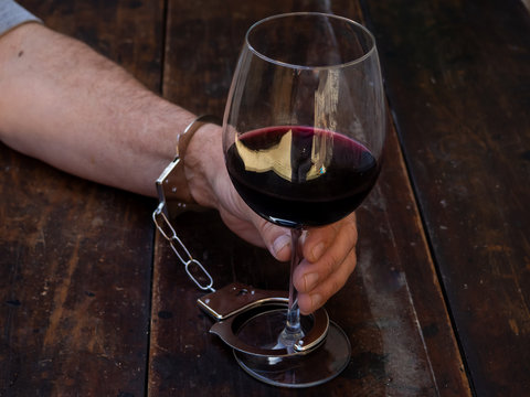 A man handcuffed to a glass of red wine. Alcohol addiction or alcoholism concept