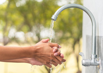 Man washing hand after working with outdoor faucet sink, cleaning hygiene protection concept with flowing water and green forest background