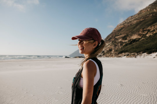 South Africa, Western Cape, Noordhoek Beach, smiling young woman wearing base cap standing on the beach