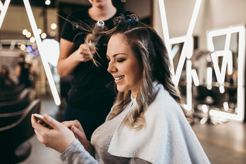 Beautiful woman with long hair at the beauty salon using smart phone and choosing hairstyle while...