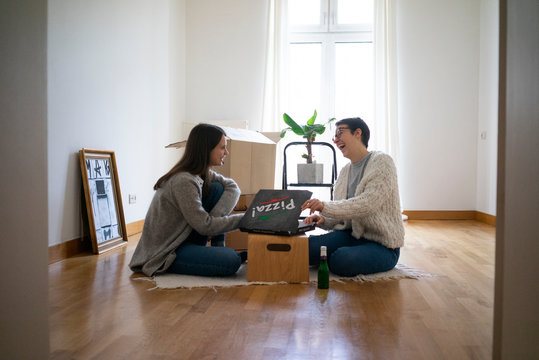Young women sitting on floor of their new home, eating pizza