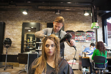 Caucasian woman having her hair styled in a hipster barbershop themes of hairstylist pampering glamour haircare