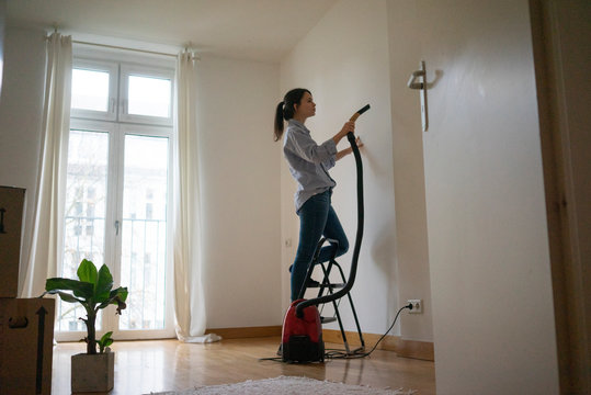 Young woman standing on step ladder, hoovering her new home