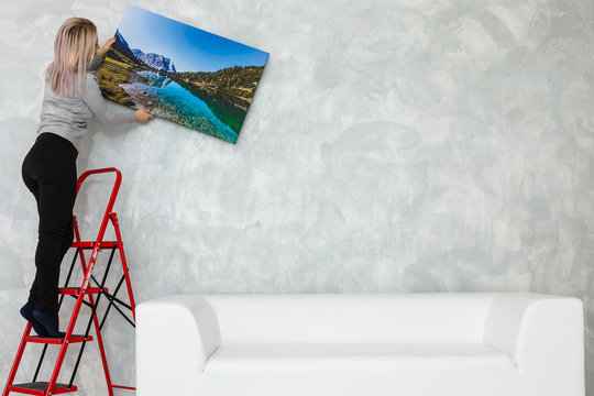 Long-haired Girl Hanging Pictures In Frames On Wall At House