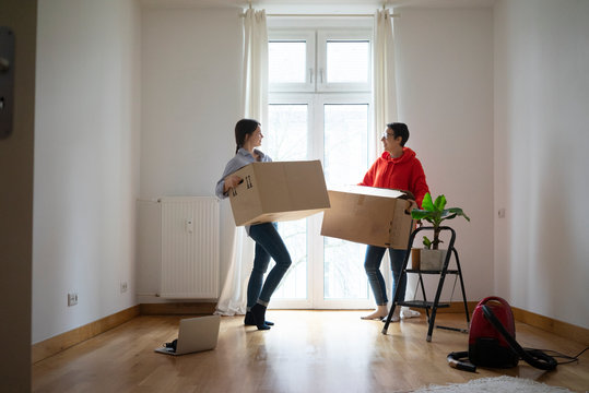 Young women moving into their new home, carrying cardboard boxes