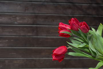 Fototapeta na wymiar Bouquet of red tulips on a dark brown wooden background. Festive concept. Space for copy space.