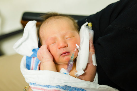 Newborn baby girl wrapped in blanket with IV in her hand