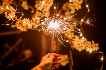 Glittering sparklers against the background of spring flowers of trees. Spring time.