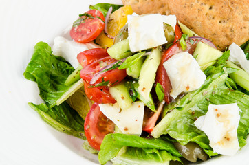 Greek salad with feta cheese, Ligurian olives and tortilla pea and hummus on a plate on a white background, close up